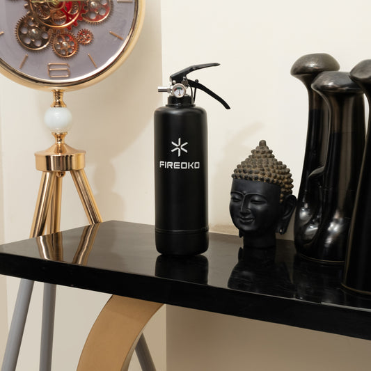 Black fire extinguisher with 'FIREOKO' branding on a table with decorative items.