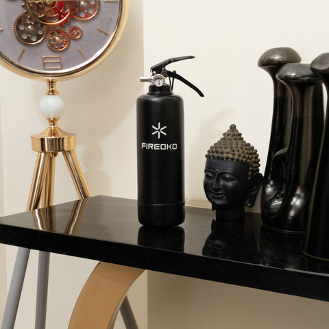 Black fire extinguisher with 'FIREOKO' branding on a table with decorative items.